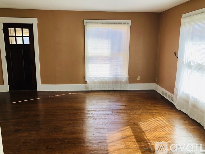 A room with wooden floors and a window with white curtains.
