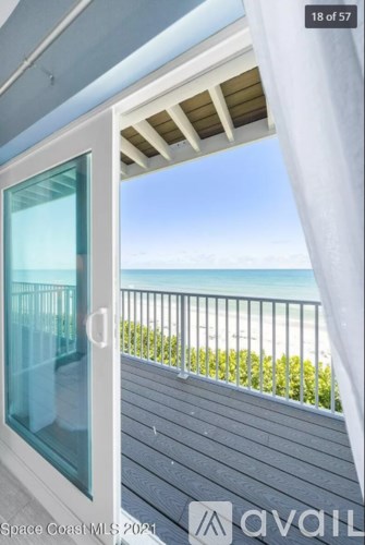 A balcony with a glass door overlooking a beach.