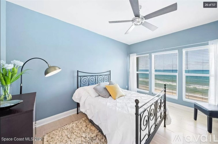 A bedroom with a bed, a ceiling fan, and a window overlooking the beach.
