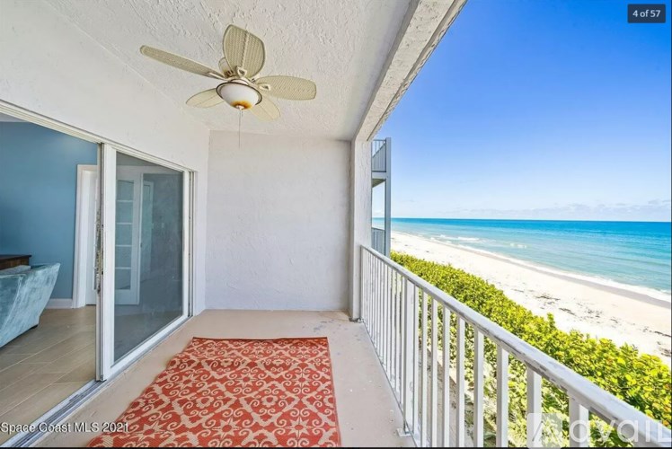 A balcony with a red carpet and a ceiling fan overlooking the beach.