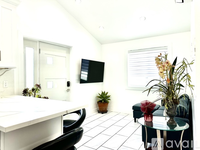 A white kitchen with a black chair and a glass table with a vase of flowers on it.