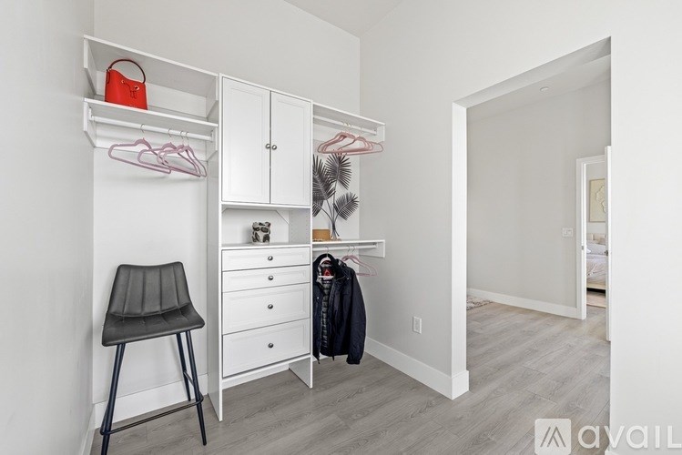 A room with a white chair and a white cabinet with a red bag on top.