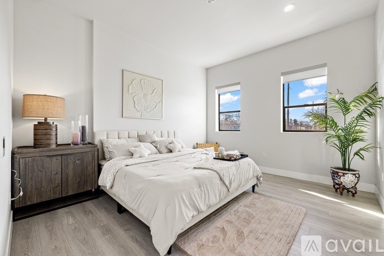 A bedroom with a large bed, a lamp, a plant, and a framed picture on the wall.