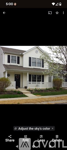 A white house with a brown roof and a tree in front.