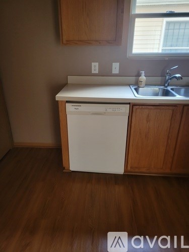 A white dishwasher is in a kitchen with wood cabinets.