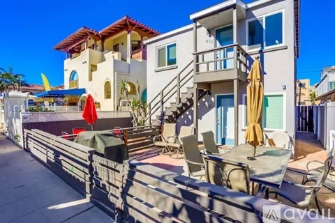 A modern two-story house with a balcony and a patio with chairs and umbrellas.