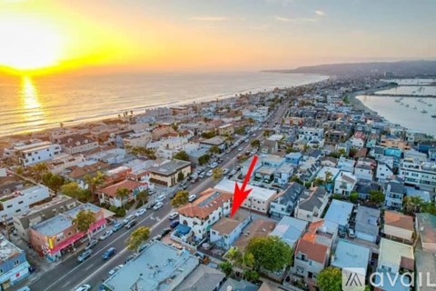 A sunset view of a coastal town with a red arrow pointing to a specific building.