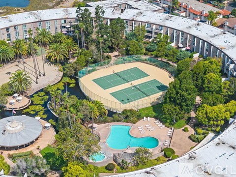 A large outdoor tennis court is surrounded by trees and buildings.