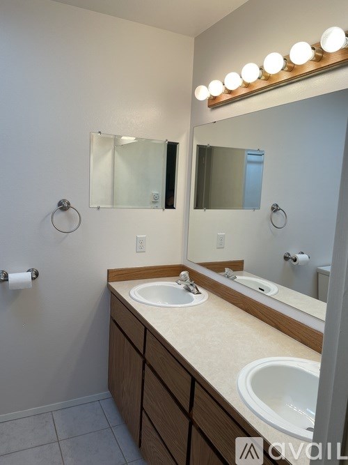 A bathroom with a vanity, two sinks, and lights above the mirror.