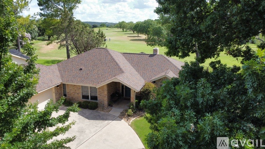 A house with a brown roof and a driveway is surrounded by trees.