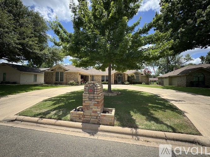 A brick pillar in front of a house with a tree in the background.