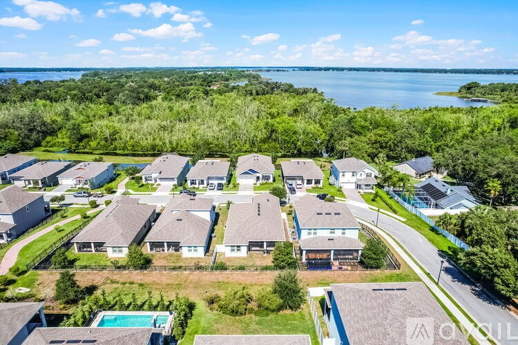A bird's eye view of a residential area with houses, a pool, and a body of water in the distance.
