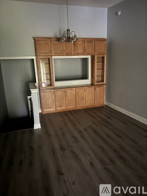 A wooden entertainment center with a television and a chandelier hangs in a room with wooden flooring.