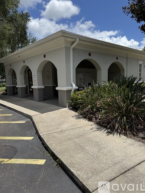A white building with arched doorways and windows is surrounded by a parking lot.
