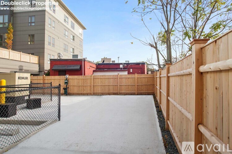 A wooden fence surrounds a concrete area with a black gate in front of a building.