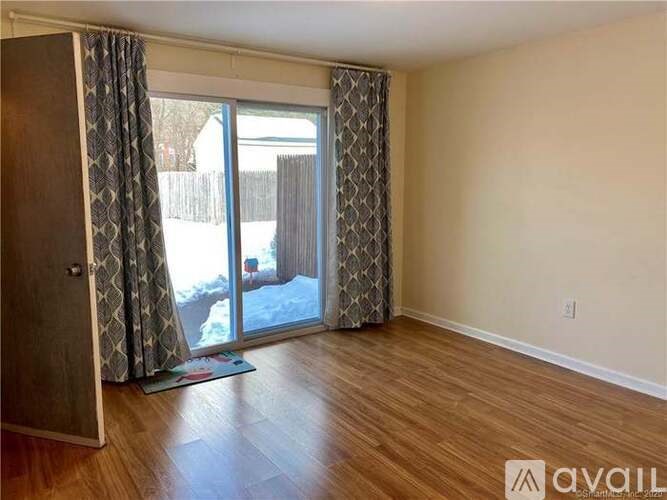 A room with wooden floors and a sliding glass door with curtains.