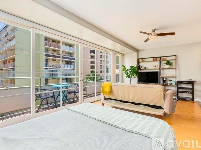 A bedroom with a bed, a couch, a television, and a balcony with a table and chairs.