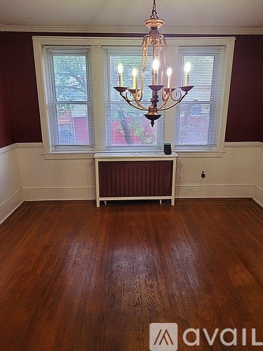 A room with a chandelier, a window with blinds, and a radiator on the wall.