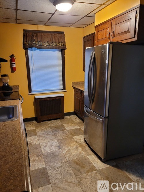 A kitchen with a black refrigerator and a window with blinds.