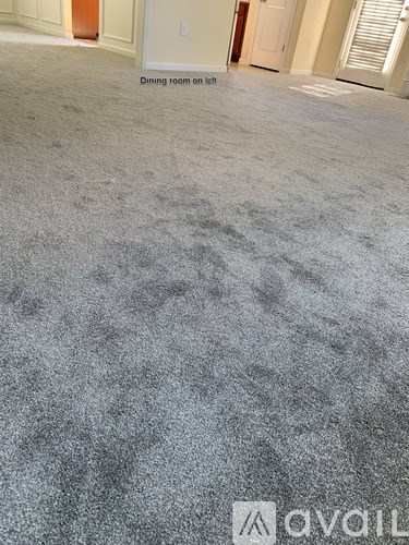 A carpeted room with a dining room on the left.