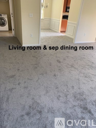 A carpeted room with a washing machine in the corner and a sign that says "Living room & sep dining room".