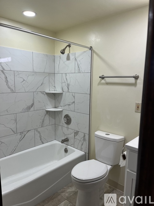 A white toilet sits next to a bathtub in a bathroom with marble tile walls.