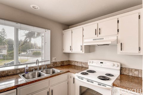 A white stove is in a kitchen with white cabinets.