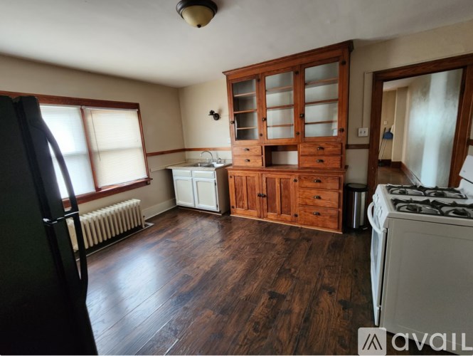 A kitchen with a black refrigerator, wooden floors, and a large wooden cabinet.