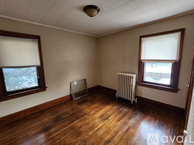 A room with wooden floors and two windows with blinds.