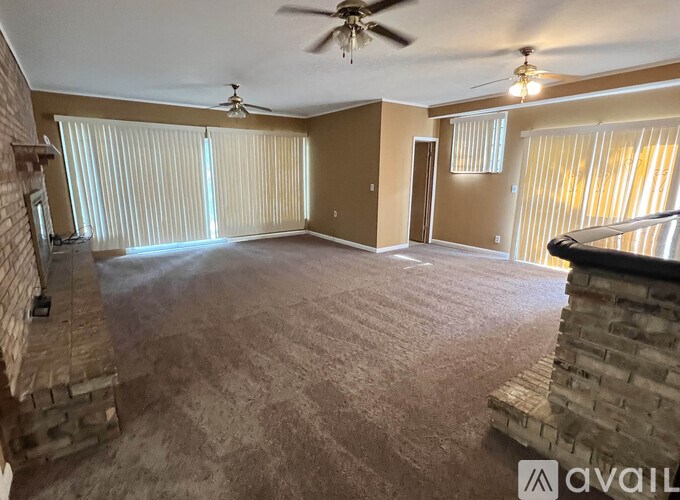 A spacious room with a carpeted floor, a ceiling fan, and a stone fireplace.