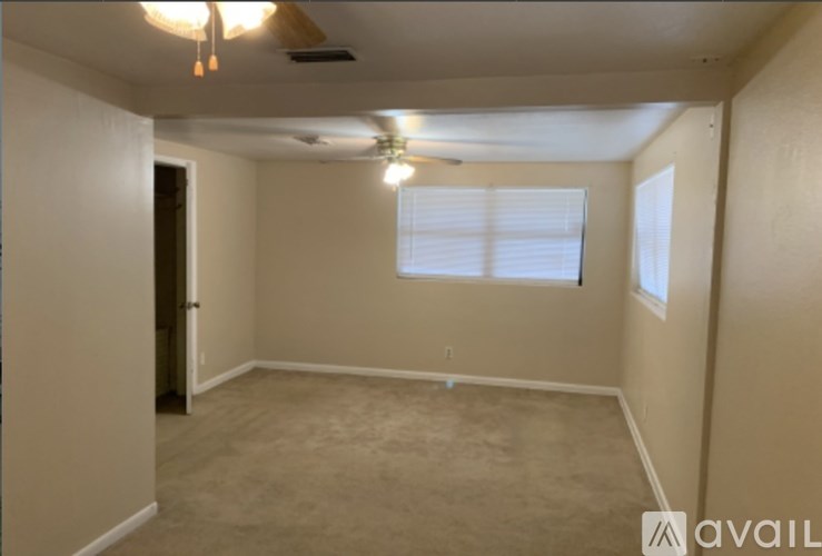 A room with a carpeted floor, a ceiling fan, and a window with blinds.