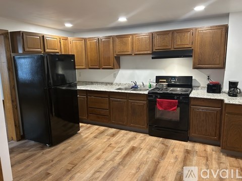 A black refrigerator stands in a kitchen with wooden cabinets and a black stove.