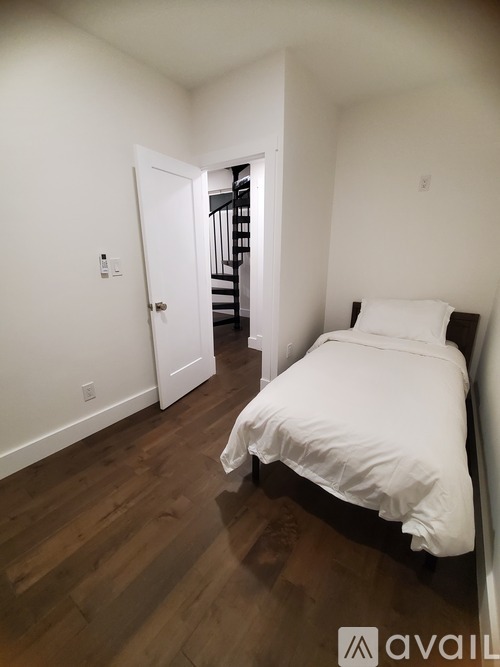 A bedroom with a bed, wooden floors, and a staircase in the background.