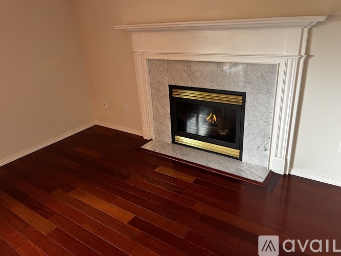 A fireplace with a white mantle and a black firebox sits in a room with wooden flooring.