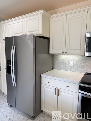 A stainless steel refrigerator with a white door stands in a kitchen with white cabinets.