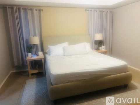 A bedroom with a large bed, two lamps, and a nightstand with a plant.