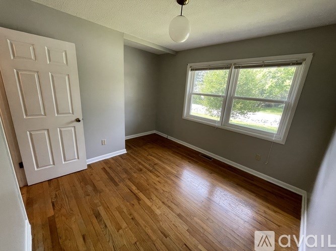 A room with a white door and a window with a view of trees outside.