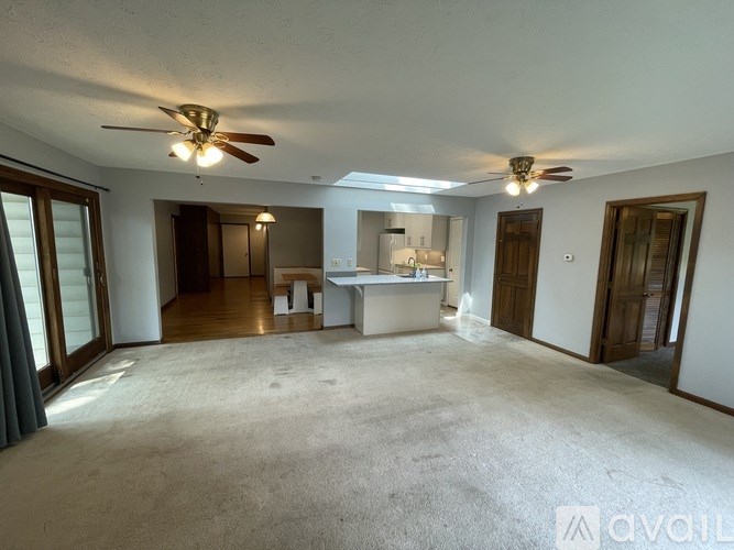 A spacious living room with a ceiling fan and a kitchen area in the background.