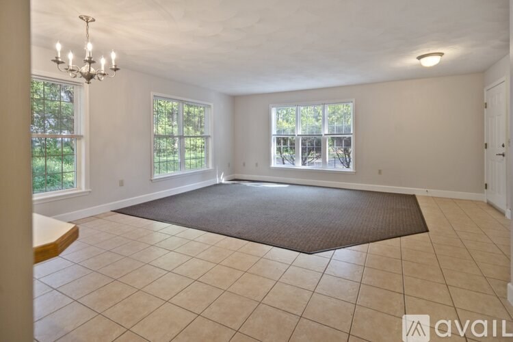 A large, empty room with a chandelier, tiled flooring, and large windows.