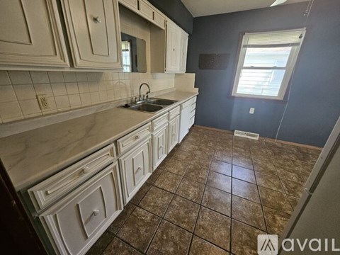 A kitchen with white cabinets and brown tiles.