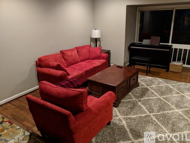 A living room with a red couch and a piano.