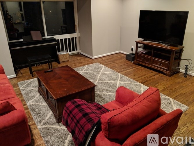 A living room with a piano, red chairs, and a television.