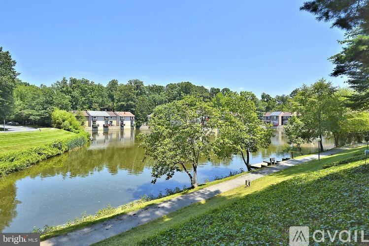 A serene landscape with a lake, trees, and a house in the distance.