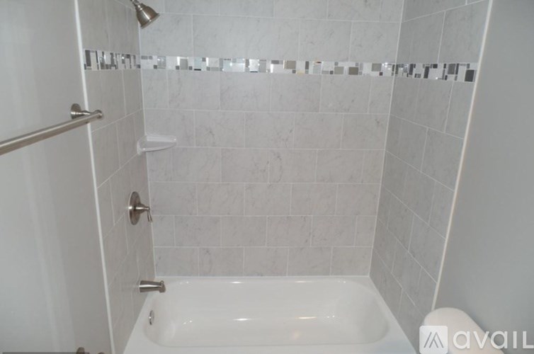 A white tiled shower with a white tub and a silver shower head.