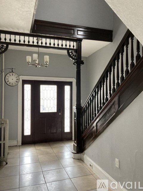 A staircase with a wooden banister and a chandelier hangs over a tiled floor.