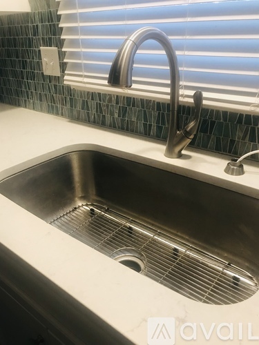 A kitchen sink with a chrome faucet and a window with blinds in the background.