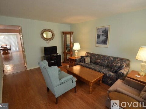 A living room with a grey sofa, a wooden coffee table, a grey armchair, a wooden side table with a lamp, a wooden cabinet, a TV, a mirror, and a painting on the wall.