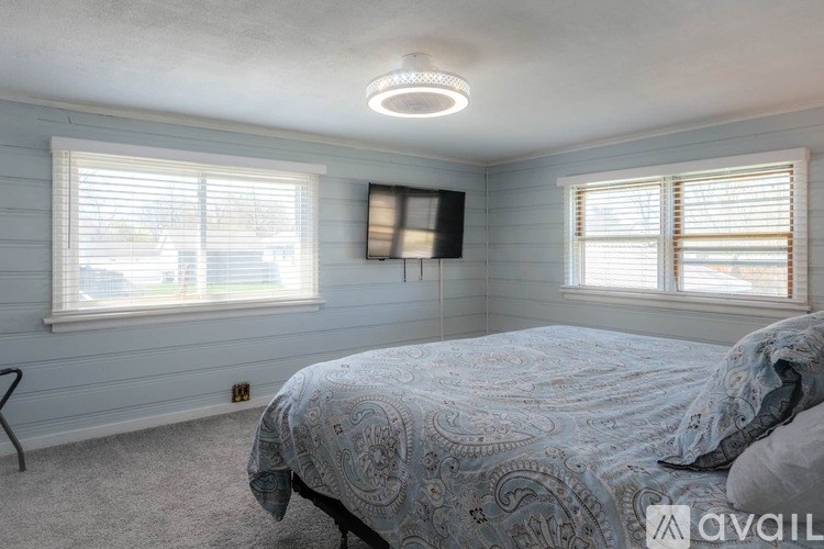 A bedroom with a bed, a television, and two windows.