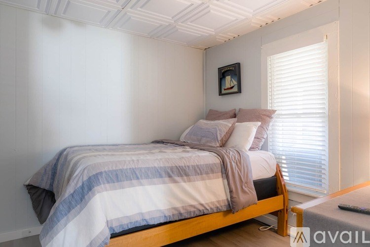 A bedroom with a bed, a window with blinds, and a picture on the wall.