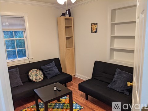 A living room with two black couches and a wooden bookshelf.